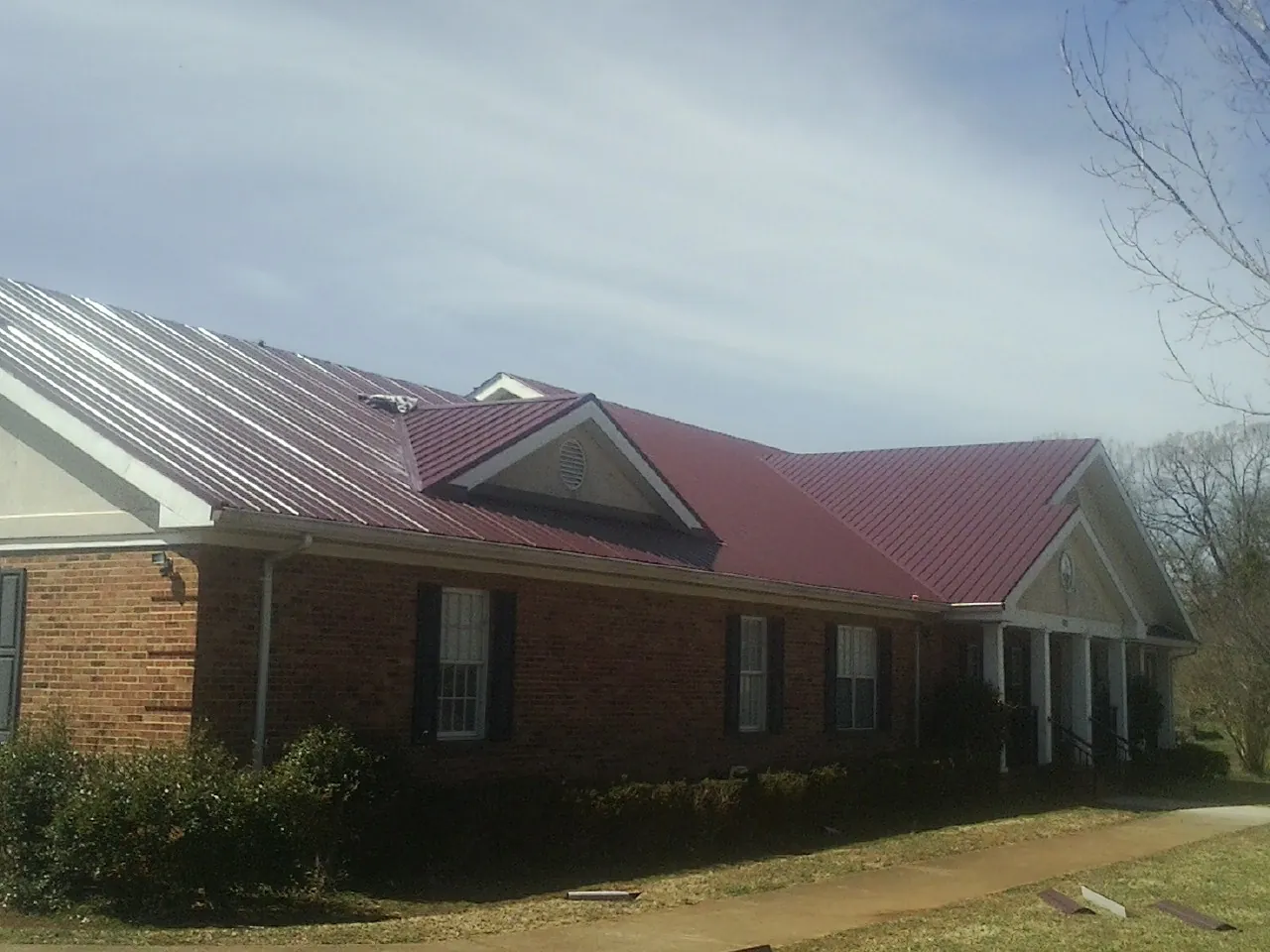 Red metal roof with gabled entries on a long brick building, from a Hail Damage Roof Repair job in Centerville